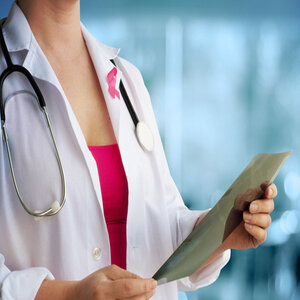 Femaile doctor wearing a white lab coat and a pink shirt with pink ribbon on coat.