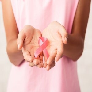 Female wearing a pink shirt holding a pink ribbon.