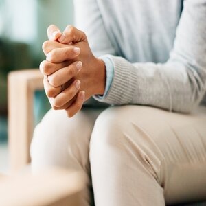 Female clasping her hands together while sitting in a chair.